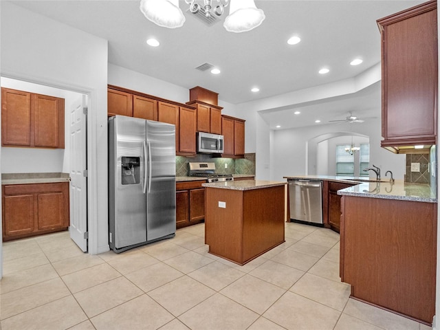 kitchen with backsplash, hanging light fixtures, light stone countertops, a kitchen island, and stainless steel appliances