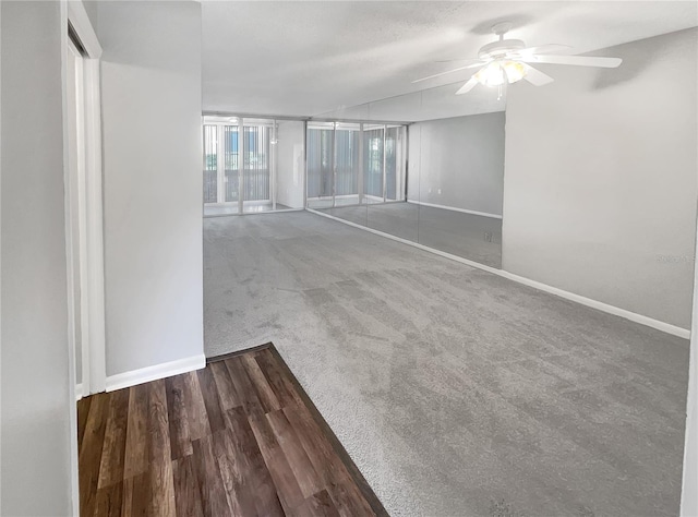 spare room featuring dark colored carpet, ceiling fan, and a wall of windows