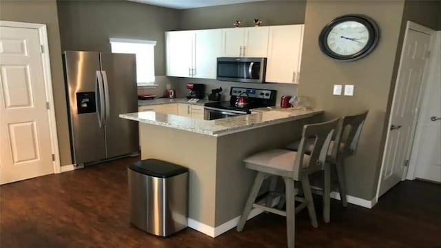 kitchen with stainless steel appliances, light stone countertops, kitchen peninsula, white cabinets, and dark hardwood / wood-style floors