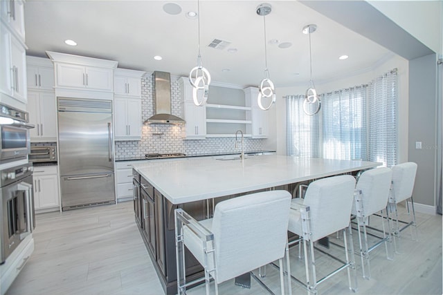 kitchen featuring pendant lighting, stainless steel appliances, wall chimney exhaust hood, white cabinetry, and backsplash