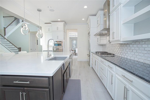 kitchen with stainless steel appliances, tasteful backsplash, wall chimney exhaust hood, white cabinets, and hanging light fixtures