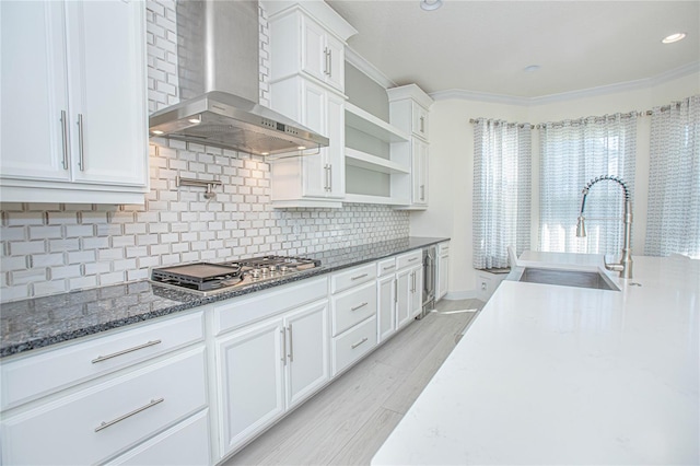 kitchen with wall chimney range hood, white cabinets, sink, and dark stone countertops