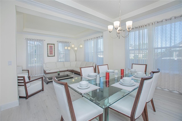 dining space with a raised ceiling, light hardwood / wood-style floors, ornamental molding, and a chandelier