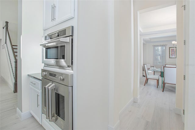 kitchen with light hardwood / wood-style floors, a notable chandelier, stainless steel double oven, white cabinets, and a raised ceiling