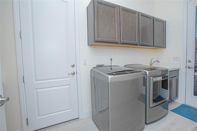 laundry area with washing machine and clothes dryer, cabinets, sink, and light hardwood / wood-style flooring