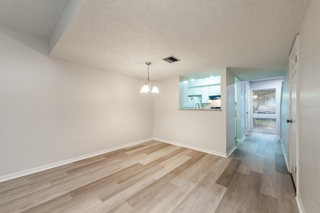 spare room with a textured ceiling, a notable chandelier, and light hardwood / wood-style flooring