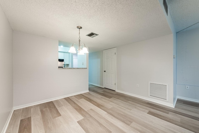 empty room with light hardwood / wood-style floors, a textured ceiling, and an inviting chandelier