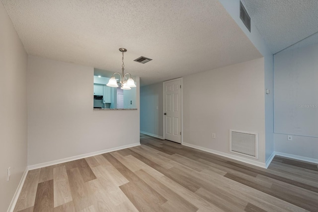 unfurnished room with light wood-type flooring, a notable chandelier, and a textured ceiling