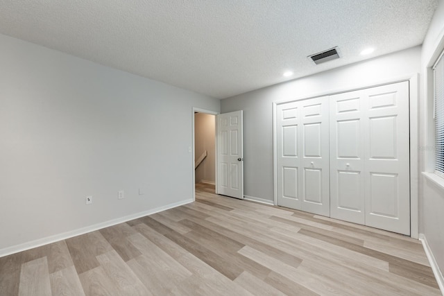 unfurnished bedroom featuring a closet, a textured ceiling, and light wood-type flooring