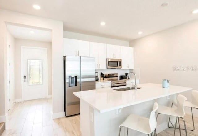 kitchen with an island with sink, sink, a kitchen breakfast bar, light hardwood / wood-style floors, and stainless steel appliances