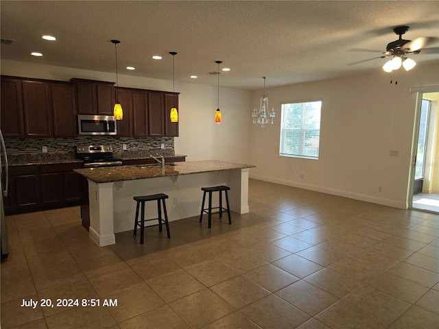 kitchen with sink, a breakfast bar, stainless steel appliances, an island with sink, and dark stone counters