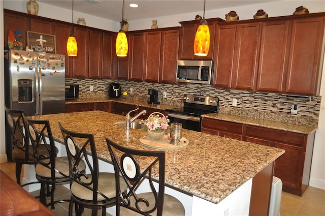 kitchen featuring appliances with stainless steel finishes, a center island with sink, and decorative light fixtures