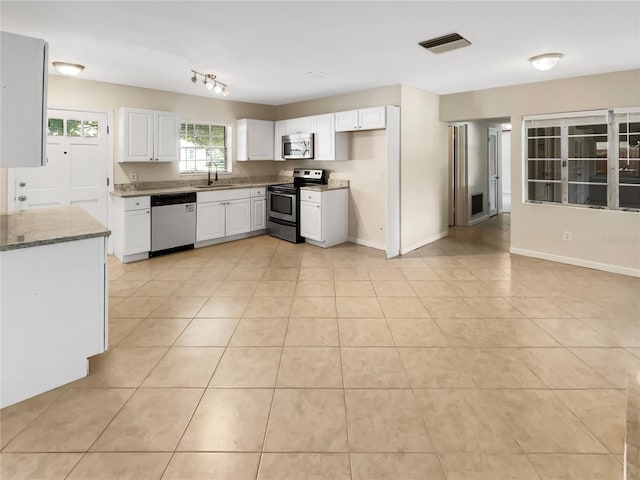 kitchen with white cabinets, sink, appliances with stainless steel finishes, light tile patterned flooring, and light stone counters