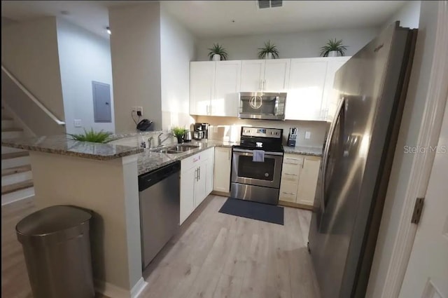 kitchen with appliances with stainless steel finishes, kitchen peninsula, light hardwood / wood-style flooring, and light stone counters