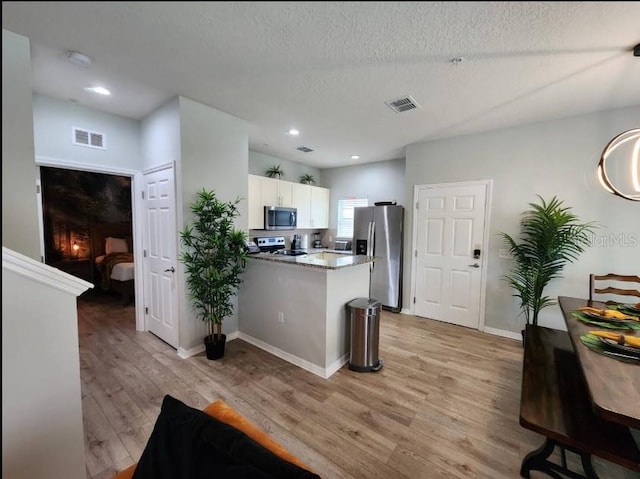 kitchen with white cabinetry, light hardwood / wood-style floors, appliances with stainless steel finishes, a textured ceiling, and kitchen peninsula