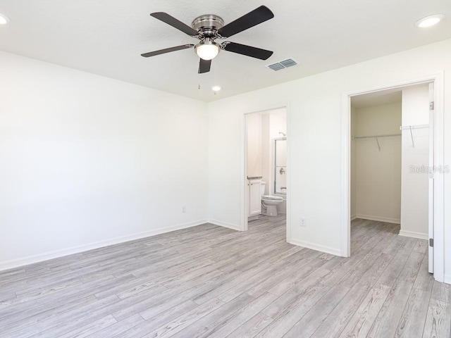 unfurnished bedroom with light wood-type flooring, ceiling fan, a spacious closet, connected bathroom, and a closet