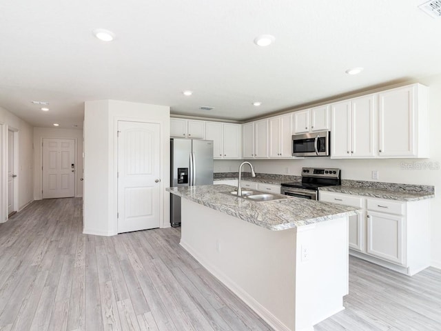 kitchen with a center island with sink, white cabinets, sink, appliances with stainless steel finishes, and light hardwood / wood-style floors