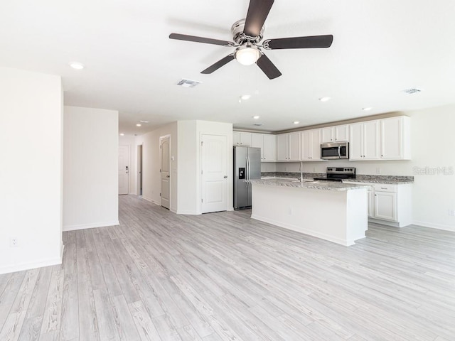 kitchen with appliances with stainless steel finishes, light stone counters, light hardwood / wood-style flooring, white cabinets, and an island with sink