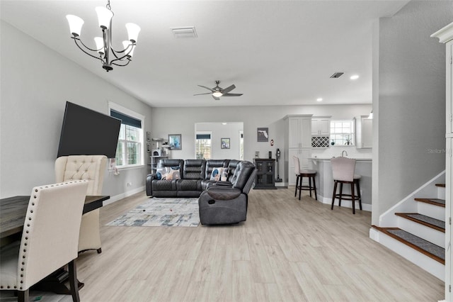 living room featuring ceiling fan with notable chandelier and light hardwood / wood-style flooring