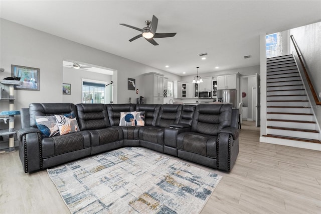 living room featuring plenty of natural light, ceiling fan with notable chandelier, and light wood-type flooring