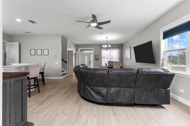 living room with ceiling fan with notable chandelier and light hardwood / wood-style flooring