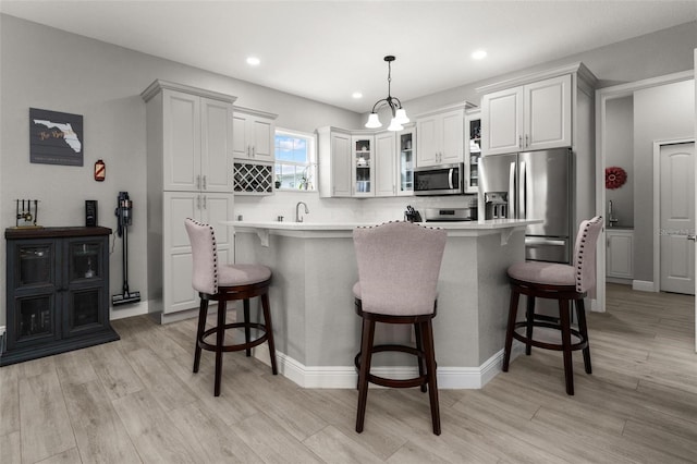 kitchen featuring stainless steel appliances, decorative light fixtures, a breakfast bar area, white cabinets, and backsplash