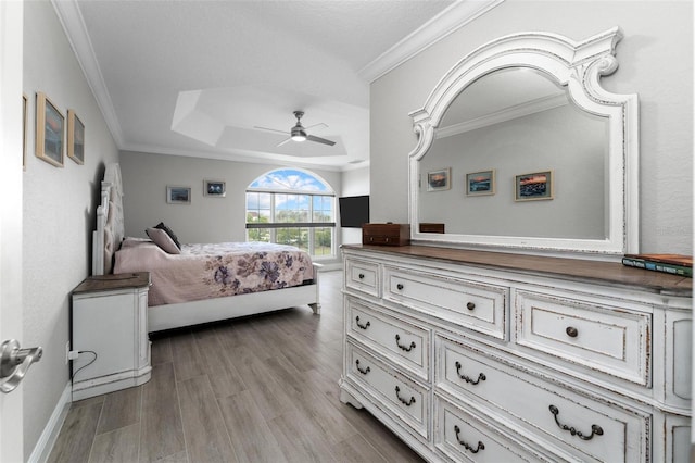 bedroom featuring a raised ceiling, ornamental molding, ceiling fan, and light wood-type flooring