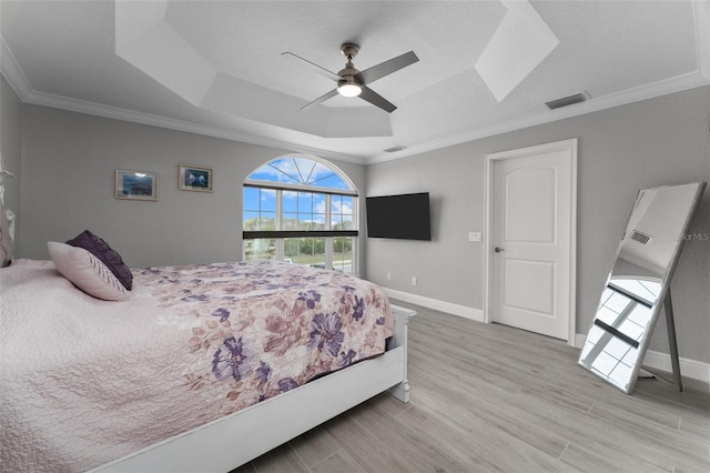 bedroom featuring light hardwood / wood-style flooring, a tray ceiling, ornamental molding, and ceiling fan