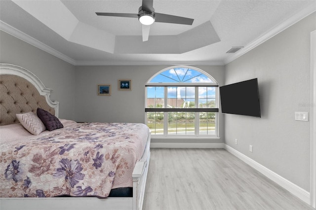 bedroom featuring ornamental molding, a tray ceiling, ceiling fan, and light wood-type flooring