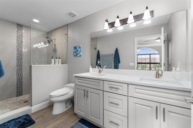 bathroom with ceiling fan, a tile shower, a textured ceiling, toilet, and double vanity