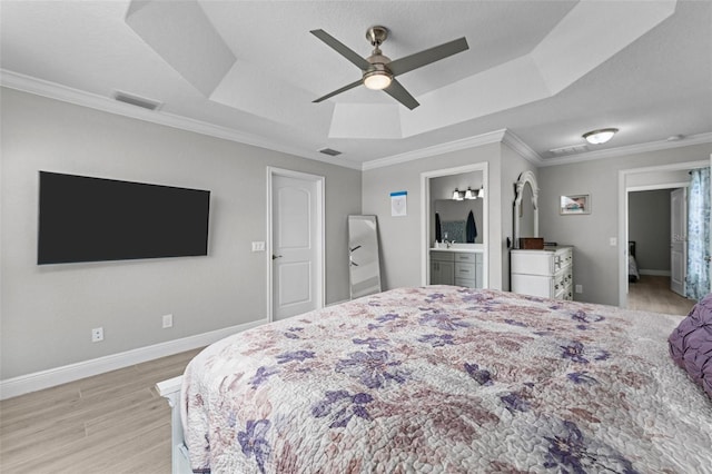 bedroom with a tray ceiling, ceiling fan, ensuite bathroom, and light hardwood / wood-style flooring