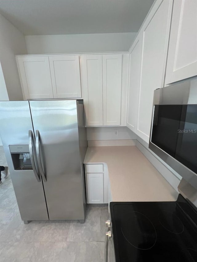 kitchen featuring light tile flooring, appliances with stainless steel finishes, and white cabinetry