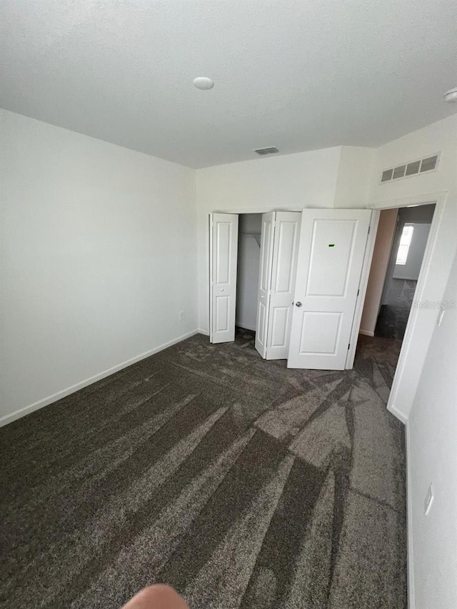 unfurnished bedroom featuring dark carpet and a closet