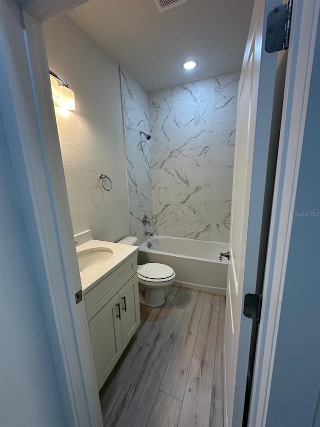 full bathroom featuring hardwood / wood-style floors, tiled shower / bath combo, vanity, and toilet