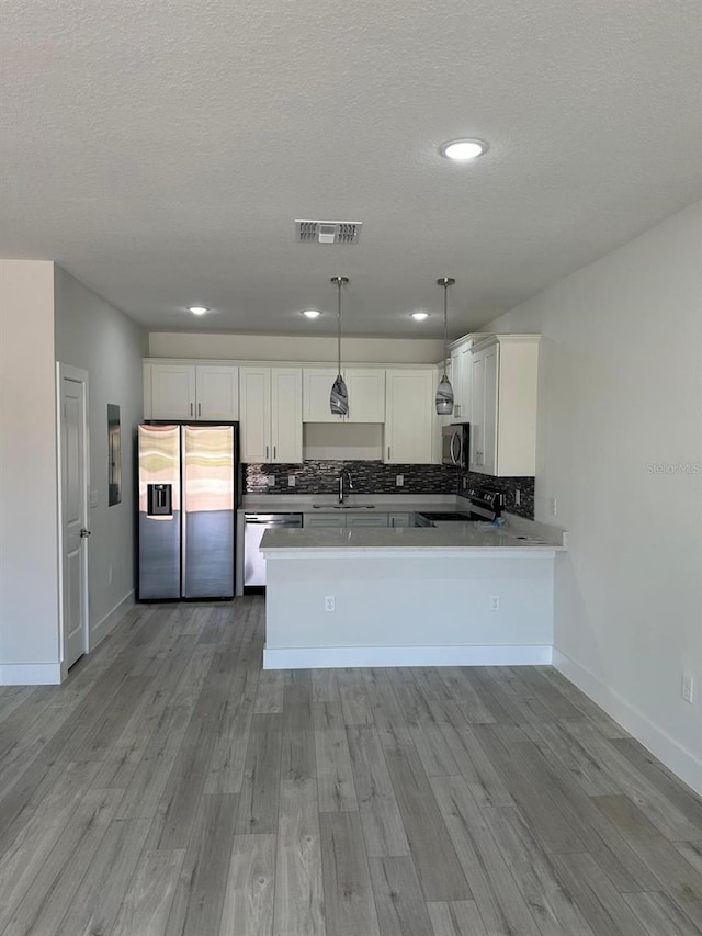 kitchen featuring appliances with stainless steel finishes, white cabinets, hanging light fixtures, and kitchen peninsula