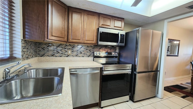 kitchen with tasteful backsplash, stainless steel appliances, light tile floors, and sink