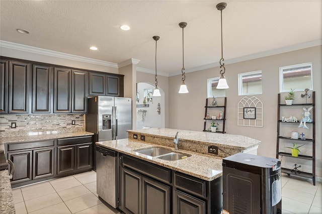 kitchen with stainless steel appliances, a center island with sink, sink, ornamental molding, and pendant lighting