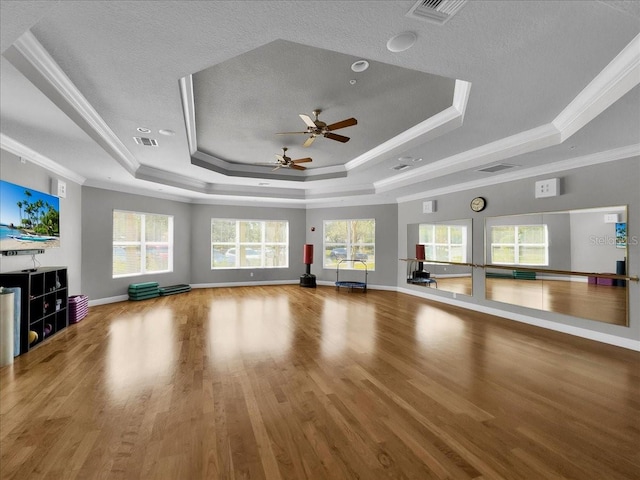 unfurnished living room featuring crown molding, ceiling fan, a tray ceiling, and light wood-type flooring