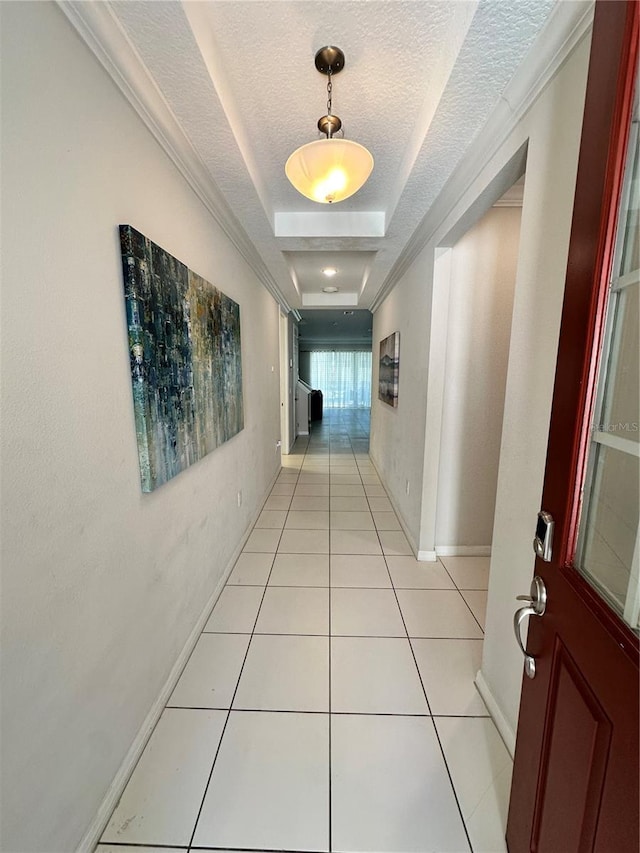 hall with ornamental molding, light tile floors, a tray ceiling, and a textured ceiling