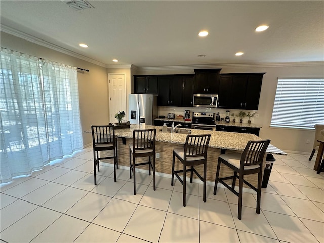 kitchen featuring light stone counters, a center island with sink, stainless steel appliances, and plenty of natural light