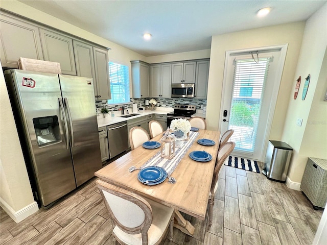 kitchen with light wood-type flooring, stainless steel appliances, sink, and backsplash