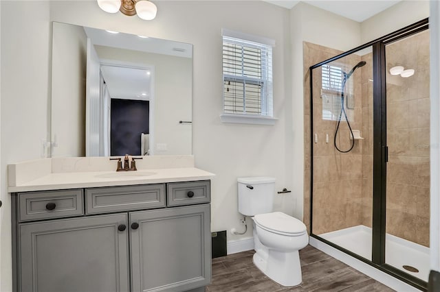 bathroom featuring wood-type flooring, toilet, vanity, and a shower with shower door