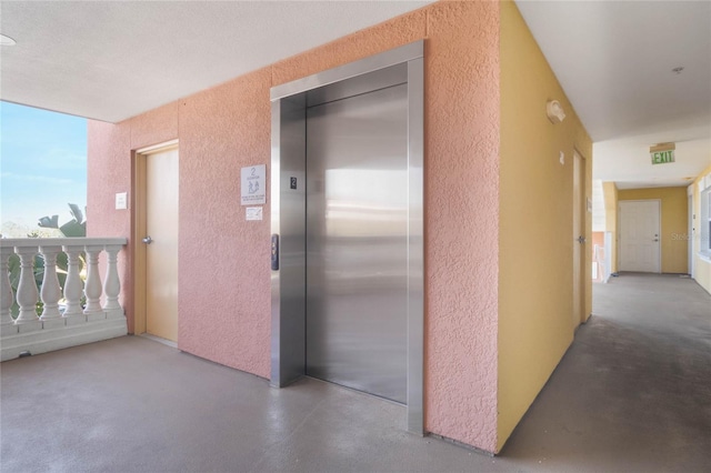 corridor with concrete flooring, elevator, and a textured ceiling