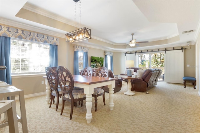 dining room with ornamental molding, a tray ceiling, light carpet, a barn door, and ceiling fan with notable chandelier