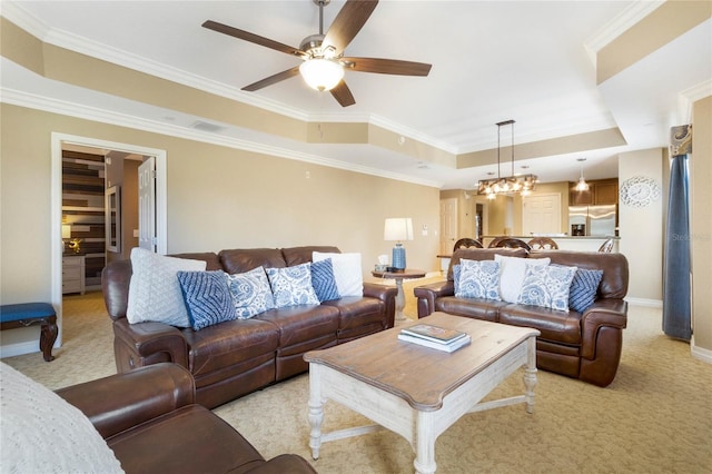 living room with ceiling fan with notable chandelier, crown molding, a raised ceiling, and light colored carpet