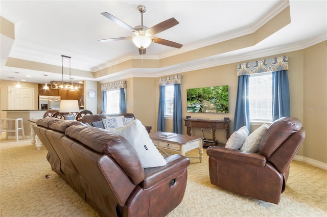 carpeted living room featuring plenty of natural light, a tray ceiling, ornamental molding, and ceiling fan with notable chandelier