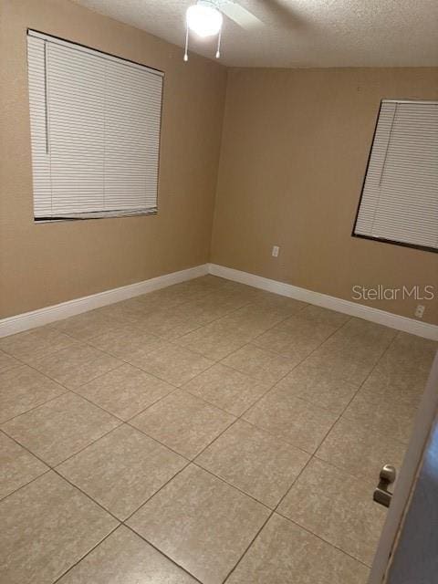 empty room featuring light tile flooring, ceiling fan, and a textured ceiling