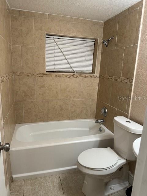 bathroom with tiled shower / bath, toilet, tile floors, and a textured ceiling