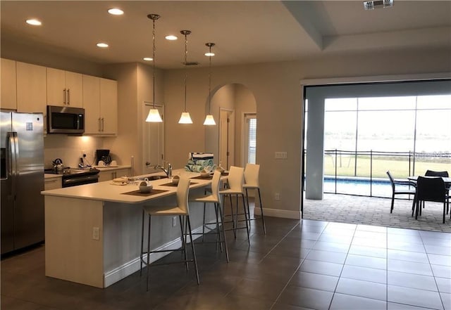 kitchen with white cabinets, stainless steel appliances, an island with sink, sink, and hanging light fixtures