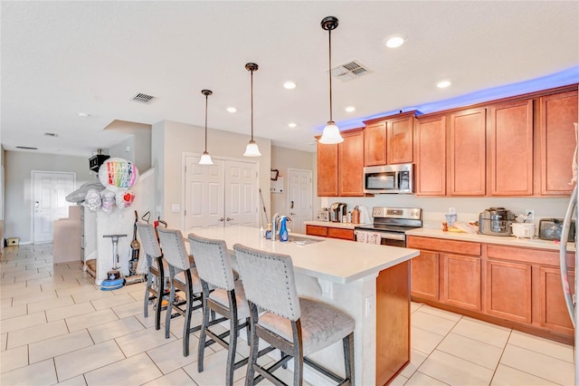 kitchen featuring an island with sink, decorative light fixtures, appliances with stainless steel finishes, and a breakfast bar